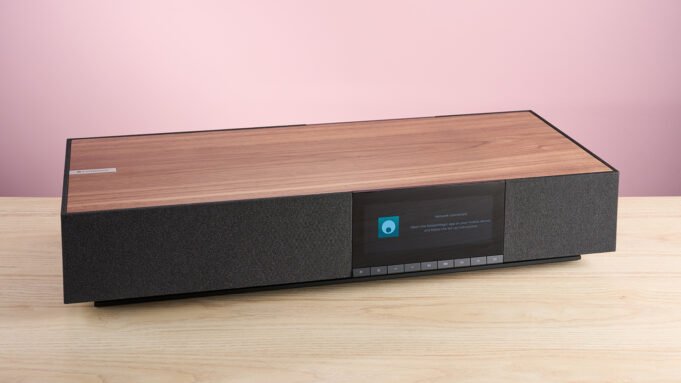 Cambridge Audio Evo One pada sudut 3/4S di atas meja kerja di depan latar belakang merah muda.