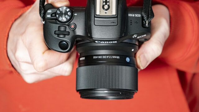 Sigma 56mm f1.4 dc dn lensa kontemporer di tangan yang melekat pada Canon EOS R100