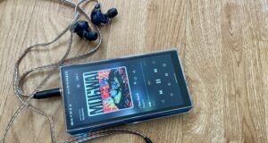 Pemain fiio m23 di tangan wanita, di atas meja kayu, bermain Mogwai, Gunna dan Fontaines DC