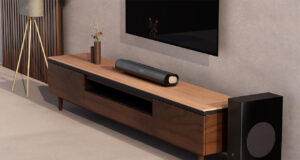 Lifestyle shot of the Creative Stage Pro soundbar on a wooden unit below a TV. The carpet and walls are a kind of oatmeal color