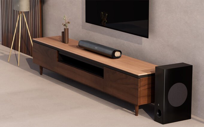 Lifestyle shot of the Creative Stage Pro soundbar on a wooden unit below a TV. The carpet and walls are a kind of oatmeal color