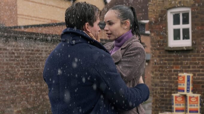 Anna and Jamie embrace in the rain outside a brick building