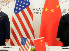 Mantan Presiden Donald Trump berpidato di podium dengan ekspresi tegas, bendera AS dan Tiongkok dipajang berdampingan di latar belakang. Simbol-simbol ekonomi seperti grafik tarif, kontainer kargo, dan panah bawah yang bersilangan menggambarkan meningkatnya ketegangan perdagangan yang dijelaskan dalam pidatonya.